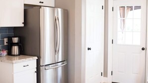 A kitchen with a stainless steel refrigerator, white cabinets, a coffee maker, and a door with a window. - Spacious Cityside House w/ Game Room & Fire Pit (Geneva)