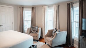 A bedroom with a bed, two armchairs, a TV, and curtains on windows. - Spacious Cityside House w/ Game Room & Fire Pit (Geneva)