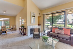 A spacious living room with a fireplace, comfortable seating, and large windows offering a view of the outdoors. - Sunny Pad w/ Patio & Pool Access in Palm Desert! (Palm Desert)