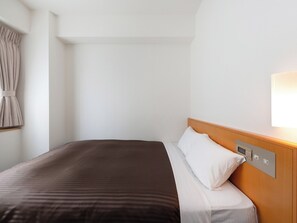 Ein Hotelzimmer mit Bett, Nachttisch, Wandlampe und einem Fenster mit Vorhängen.