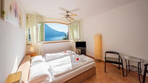 Quarto com duas camas, televisão, poltrona, mesa pequena e janela vista para o mar.