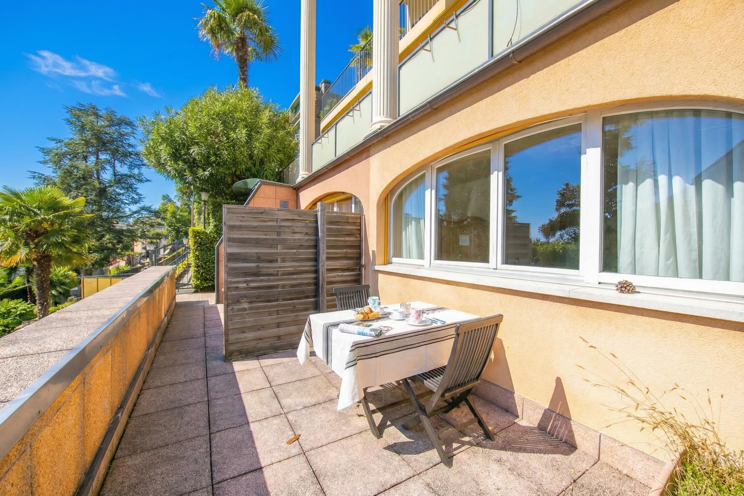 A patio with a table and chairs, a wooden fence, and a building with large windows.