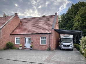 A two-story brick house with a red-tiled roof, a covered driveway, and a white truck parked in the driveway.