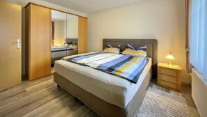 Ein Schlafzimmer mit Bett, Nachttisch, Lampe, Kleiderschrank und Spiegel.