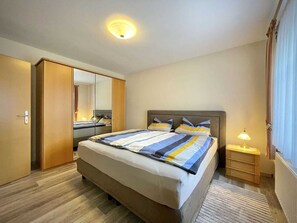 A hotel room with a large bed, a wardrobe, a bedside table with a lamp, and a mirror.