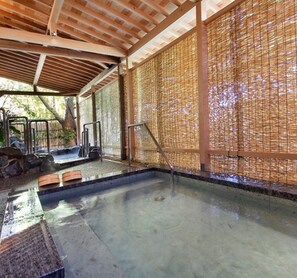 Una tradizionale onsen giapponese con tetto in legno, pavimento in tatami e parete divisoria in bambù.