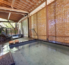 Un onsen japonés tradicional con techo de madera, suelo de esteras de tatami y pared de celosías de bambú.