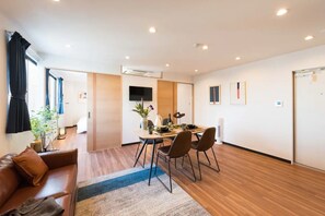 A modern hotel room with a wooden floor, a brown leather sofa, a dining table with chairs, a flat-screen TV, and a large window with curtains. - Sky Tree F Ueno Asakusa walking distance Hotel p / Sumida-ku Tokyo (Sumida-ku)