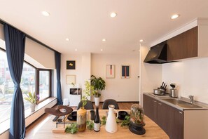 A modern kitchen with a dining area, featuring a large window, dark curtains, and a minimalist design.