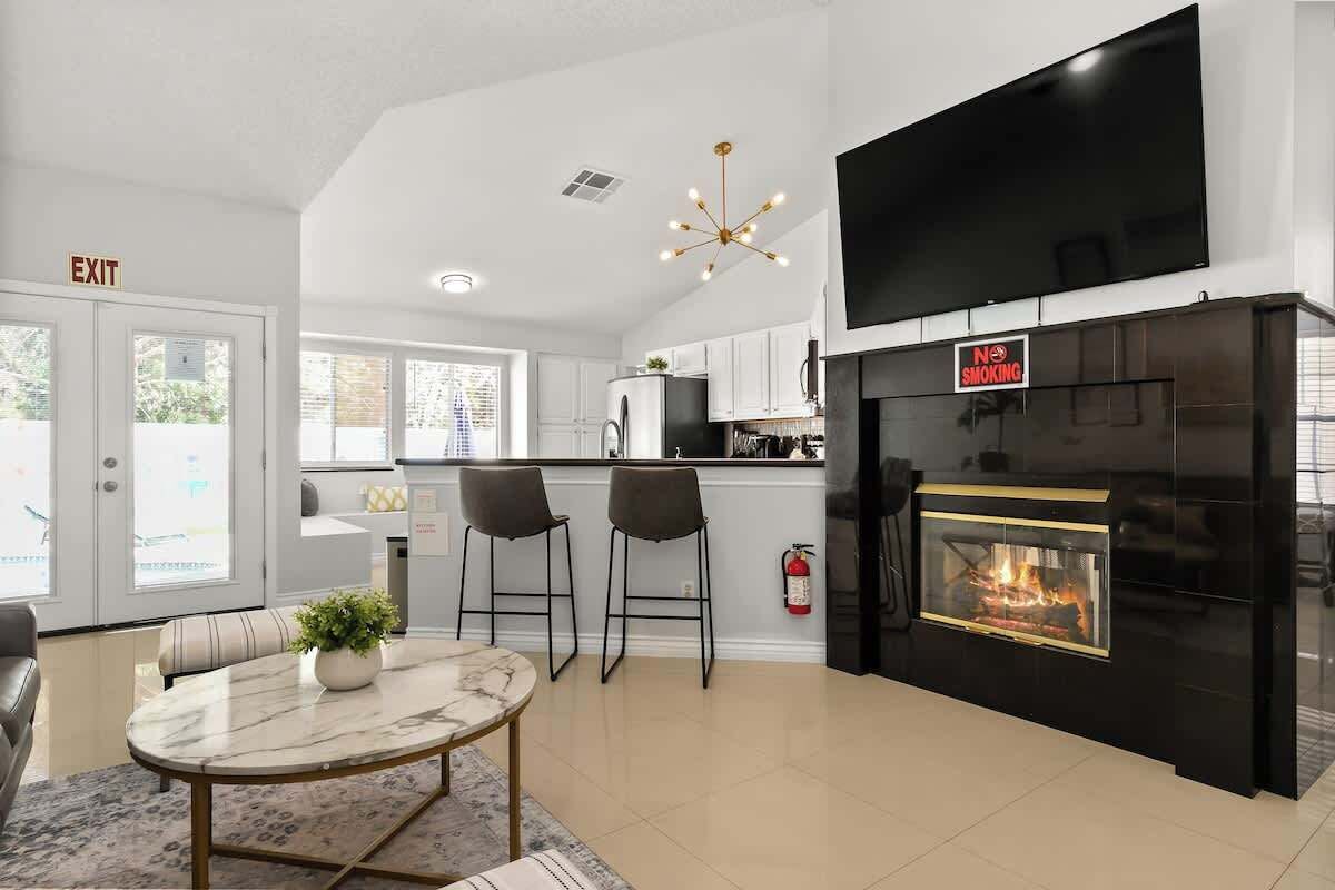 A modern kitchen with a black fireplace, white cabinets, and a flat-screen TV mounted above the counter.