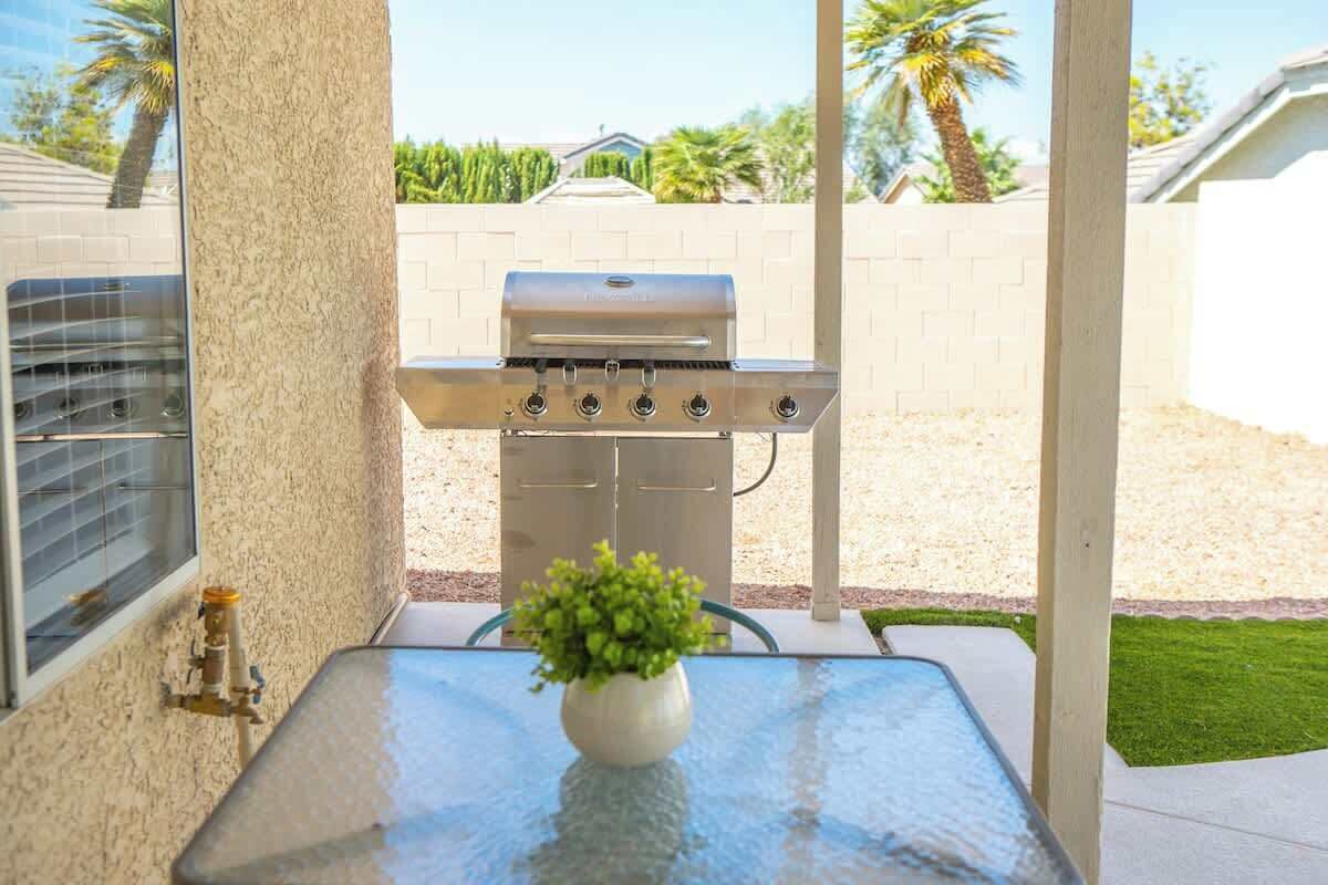 Une terrasse avec une table en verre, un barbecue et une plante en pot.