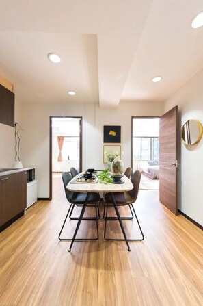 A modern kitchen with a dining area, wooden flooring, and a view through a doorway.