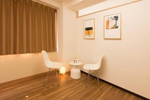 Une pièce avec un plancher en bois, deux chaises blanches, une petite table ronde et deux œuvres d’art encadrées accrochées au mur.
