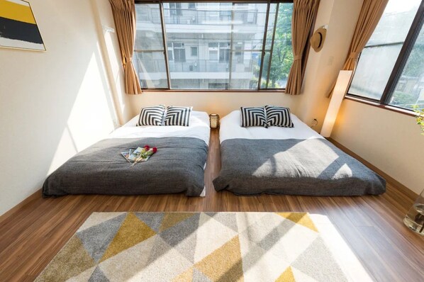 A room with two beds, a patterned rug, and a window with curtains.