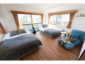 Une chambre d’hôtel avec deux lits, un canapé bleu, une petite table et une vue sur la ville.