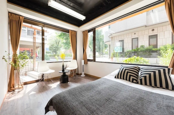 A hotel room with a bed, a chair, a small table, and a window with curtains.