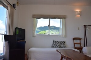A room with a bed, a TV, a window with a view of mountains, a chair, and a table.