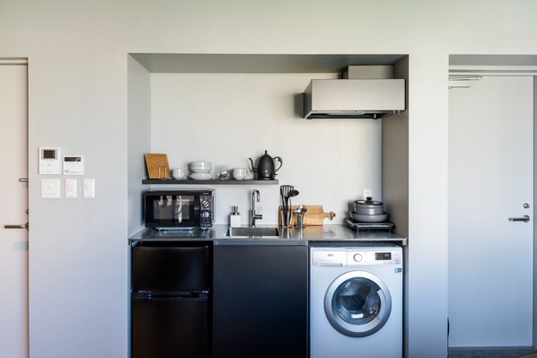 A compact kitchen with a microwave, refrigerator, washing machine, and a small sink.