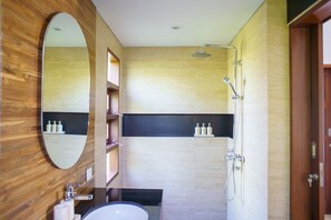 A modern bathroom with a wooden vanity, a large mirror, a shower with a handheld showerhead, and built-in shelves with toiletries.