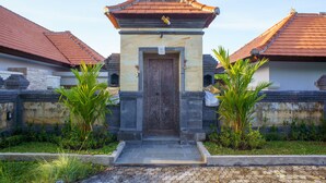 A traditional building with a central door, flanked by two palm trees, and a tiled roof. - Rapuan Cili Villa by Ilys Collection (Ubud)