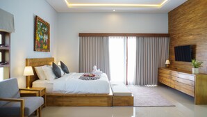 A modern hotel room with a wooden bed, a flat-screen TV, a bedside table with a lamp, and a large window with curtains. - Rapuan Cili Villa by Ilys Collection (Ubud)