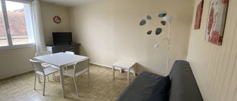 Ein Zimmer mit einer Couch, einem Esstisch mit Stühlen, einem Fernseher und Kunstwerken an den Wänden.
