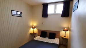 A bedroom with a bed, two bedside lamps, a window with curtains, and a wall-mounted picture.