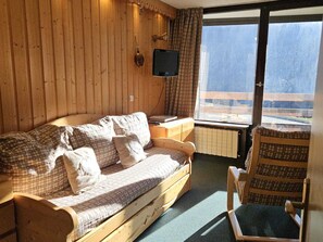 A wooden cabin room with a sofa, a television, and a view of a snowy landscape through a large window.