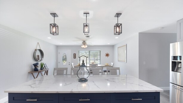 Une cuisine moderne dotée d  ’un grand îlot en marbre, de meubles de couleur sombre et de luminaires suspendus.