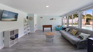 Un salon spacieux avec vue sur la piscine, comprenant un canapé, une table basse et une table de baby-foot.