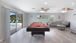 Une salle de billard équipée d’une table de billard, de ventilateurs de plafond, d’un canapé et d’une table basse.