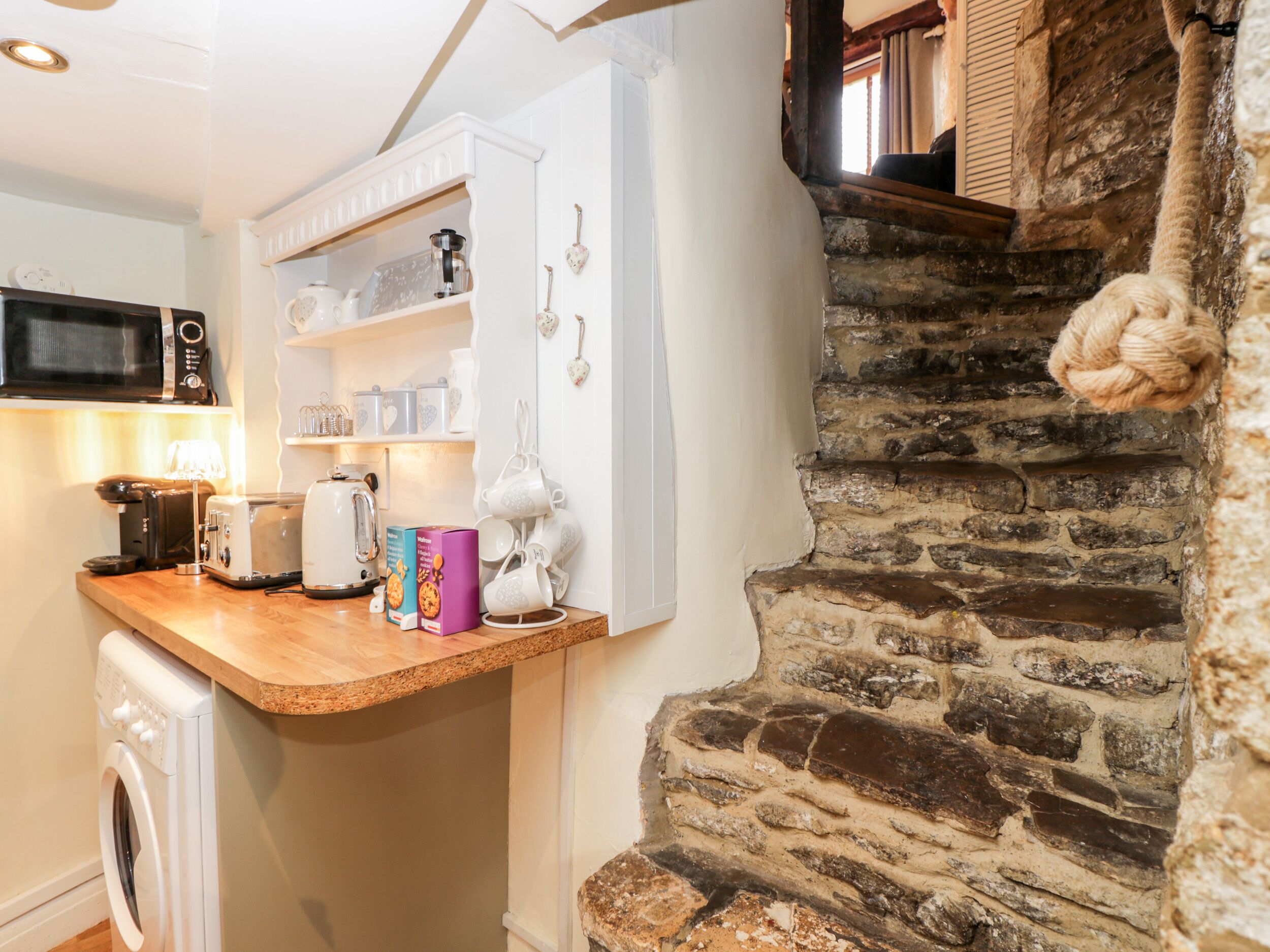 Una cocina con encimera de madera, lavadora, microondas y una escalera de piedra.