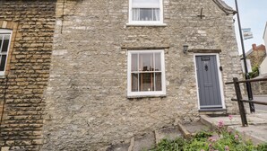 A stone building with two windows and a door, featuring a traditional architectural style. - Corner Cottage (Malmesbury)