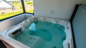 A hot tub with multiple jets, a control panel, and a view of a fenced yard through a window.