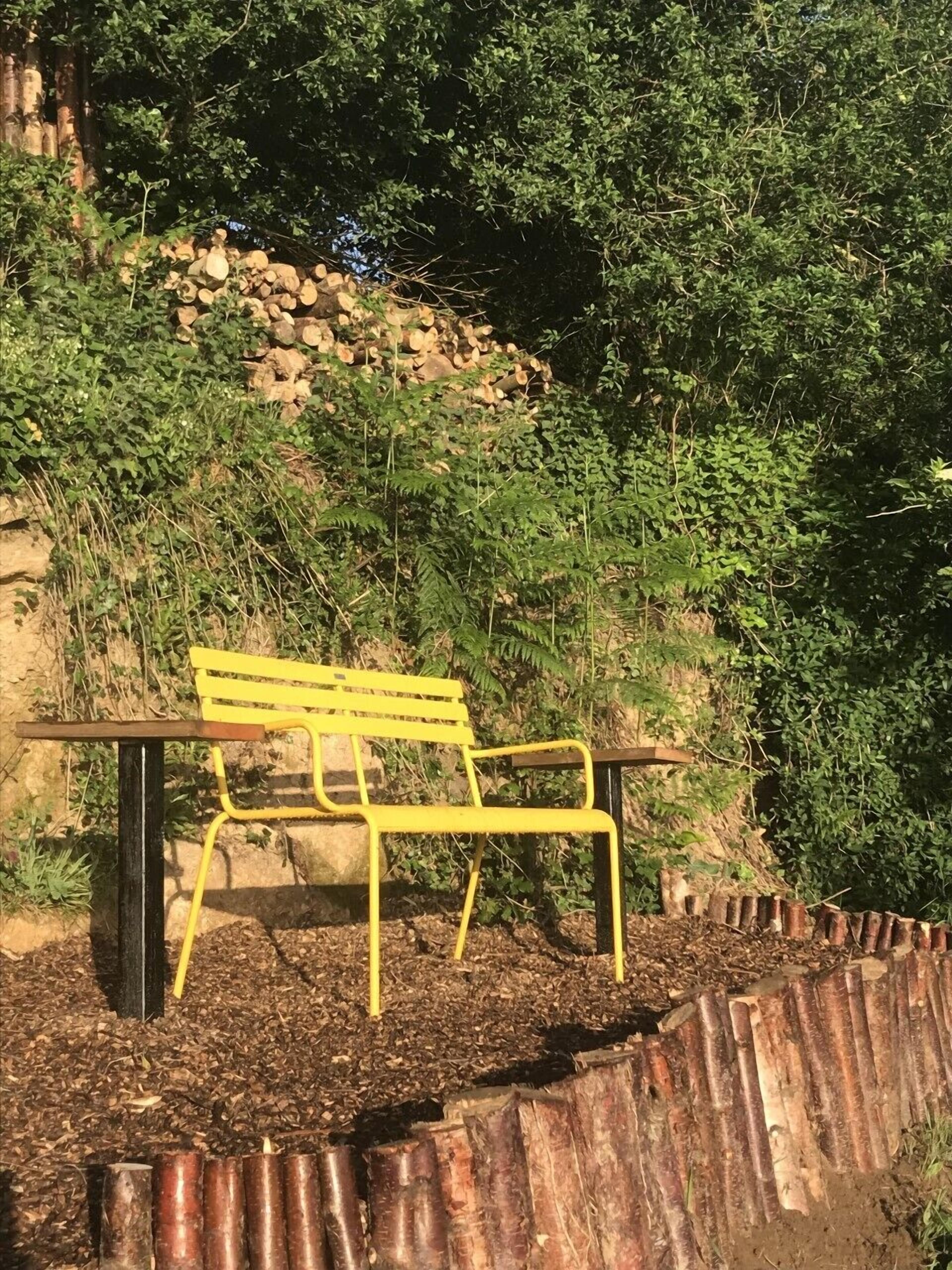 Eine gelbe Bank mit Metallgestell, auf einem Hügel aus Holzhackschnitzeln platziert.