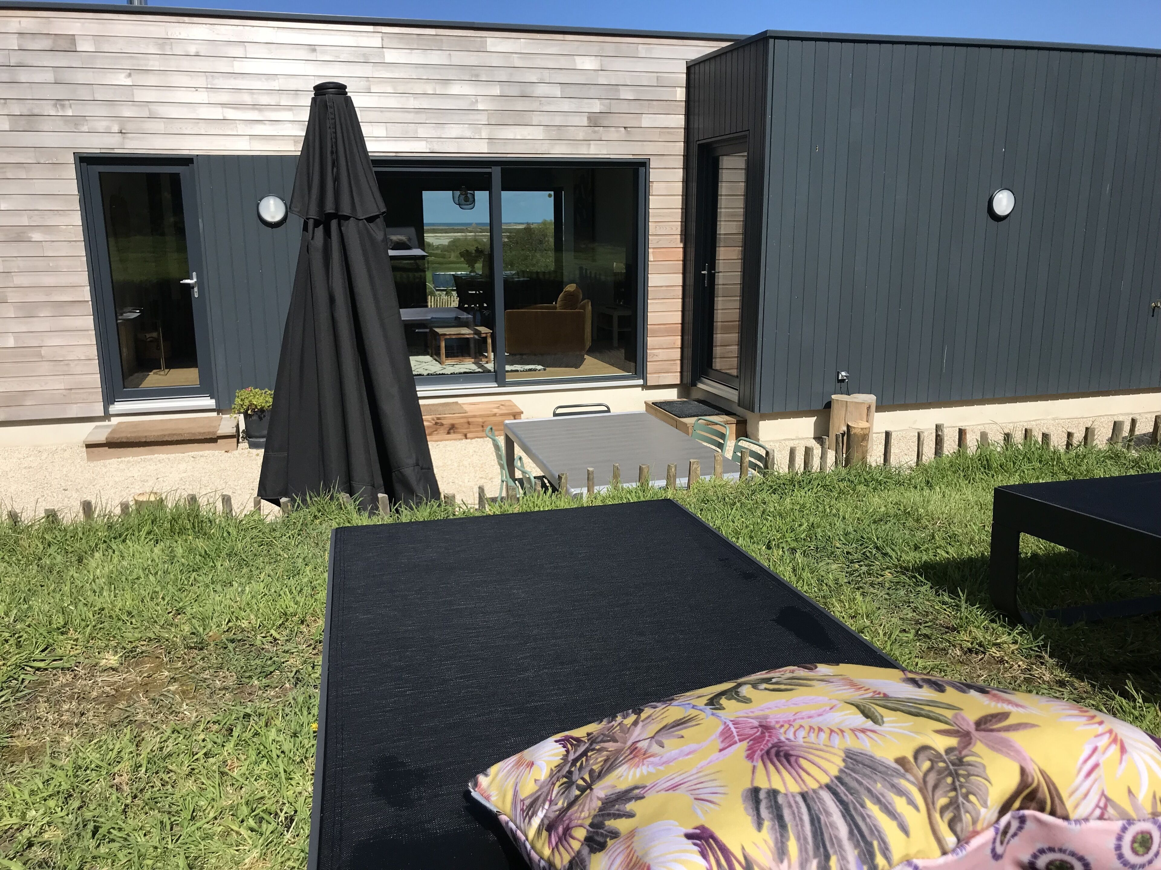 Una casa moderna con un patio que tiene una mesa negra para exteriores y una sola silla de descanso.