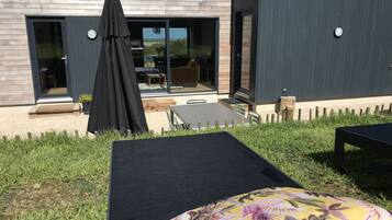 Una casa moderna con un patio que tiene una mesa negra para exteriores y una sola silla de descanso.