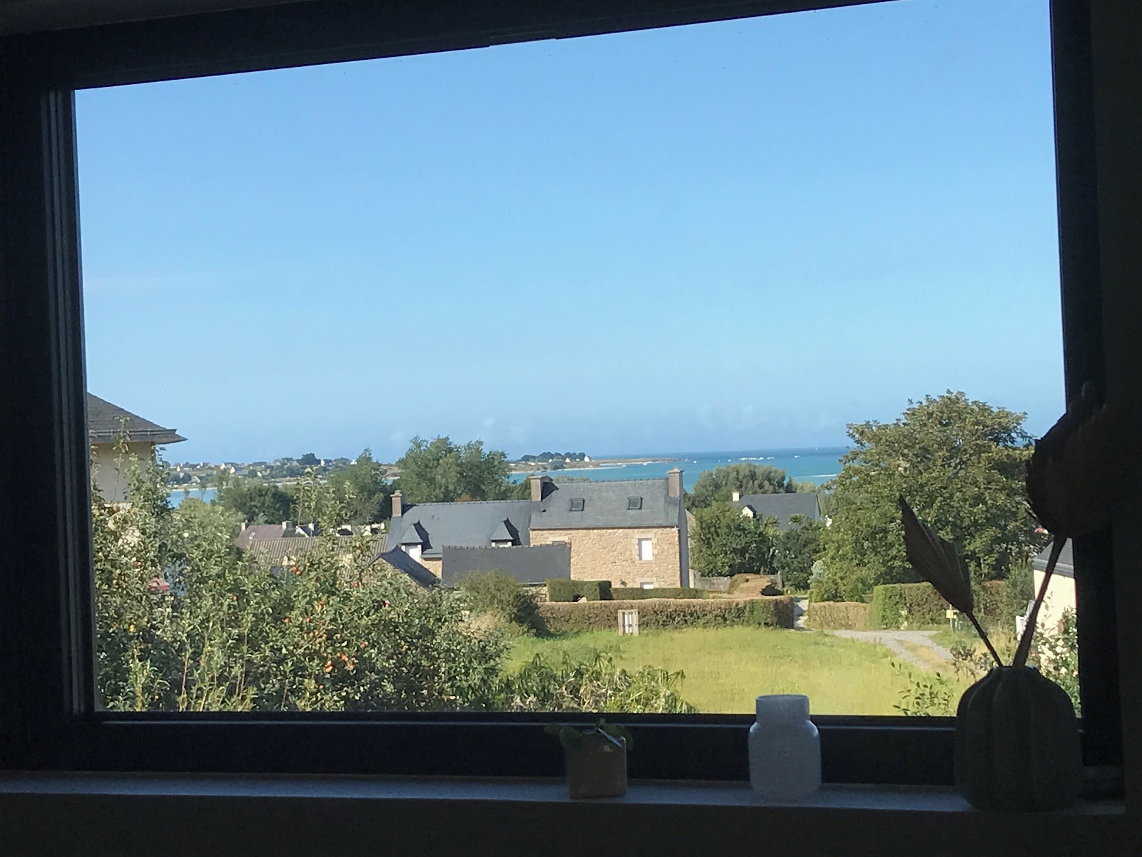 A view from a window overlooking a coastal area with houses and a clear sky.
