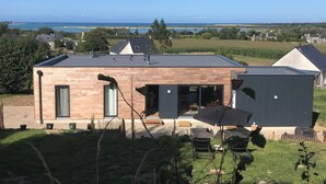 A modern two-story house with a flat roof, large windows, and a view of the sea.