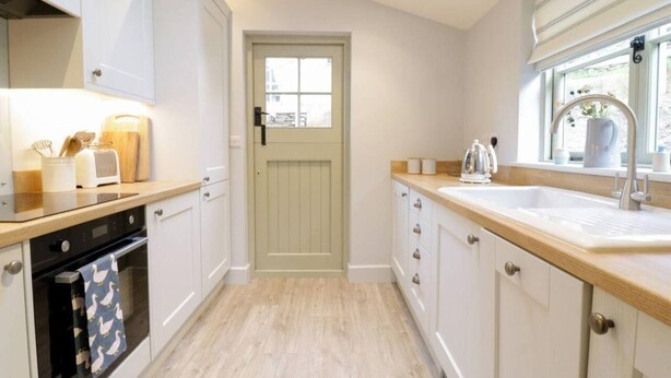 A modern kitchen with white cabinets, a wooden countertop, a built-in oven, and a window with a view. - Lovely 2-bed Cottage in Blaenau Ffestiniog (Blaenau Ffestiniog)