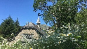 A stone building with a pointed roof and a bell tower, surrounded by lush greenery and wildflowers. - Lovely 2-bed Cottage in Blaenau Ffestiniog (Blaenau Ffestiniog)