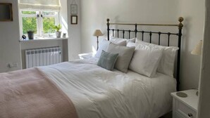 A bedroom with a bed, a nightstand, a window with a view of greenery, and a radiator. - Lovely 2-bed Cottage in Blaenau Ffestiniog (Blaenau Ffestiniog)