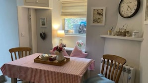 A dining area with a checkered tablecloth, a vase with flowers, and a clock on the wall. - Lovely 2-bed Cottage in Blaenau Ffestiniog (Blaenau Ffestiniog)