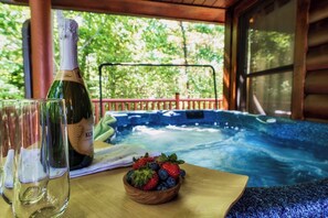 Een fles Kor wijn, een glas, en een schaal met aardbeien en blauwe bessen op een houten tafel, met een jacuzzi op de achtergrond.