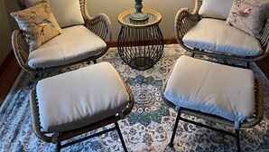 Una habitación con dos sillones de mimbre, una mesita redonda con una lámpara y una alfombra estampada.