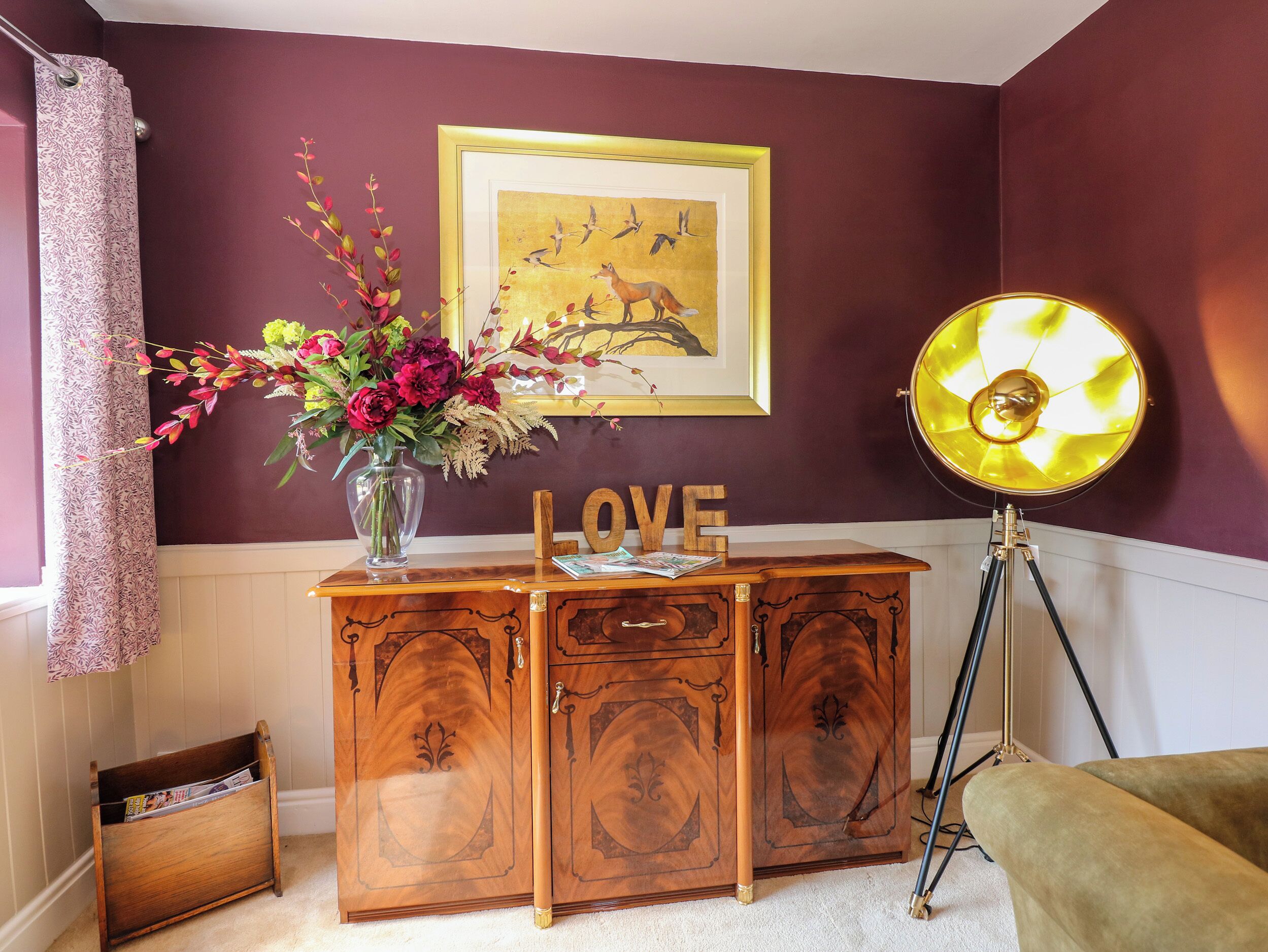 Un meuble en bois sur lequel sont posés un vase de fleurs, un tableau encadré et une lampe sur un trépied.