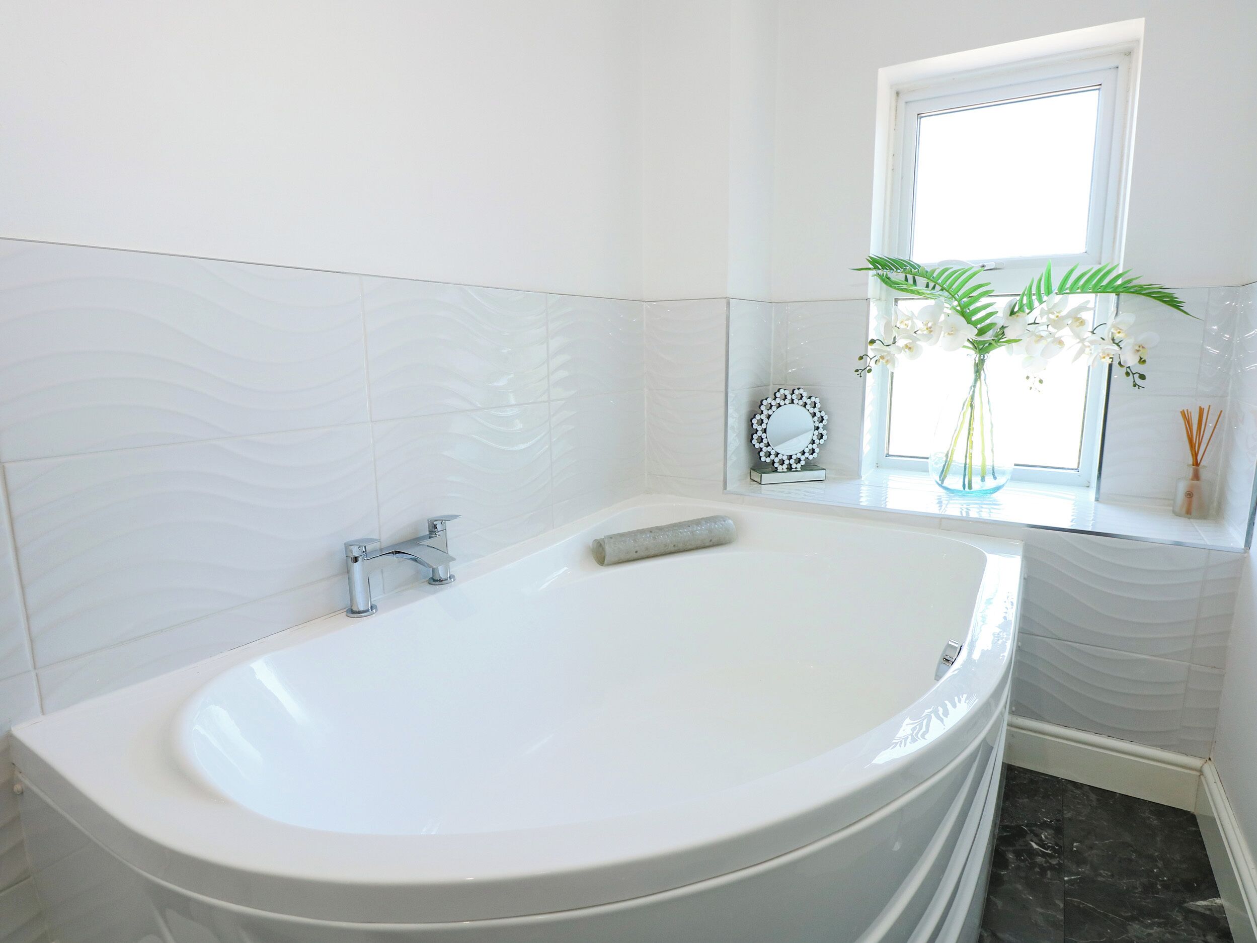 A modern bathroom with a freestanding bathtub, a vanity with a mirror, and a window with natural light.