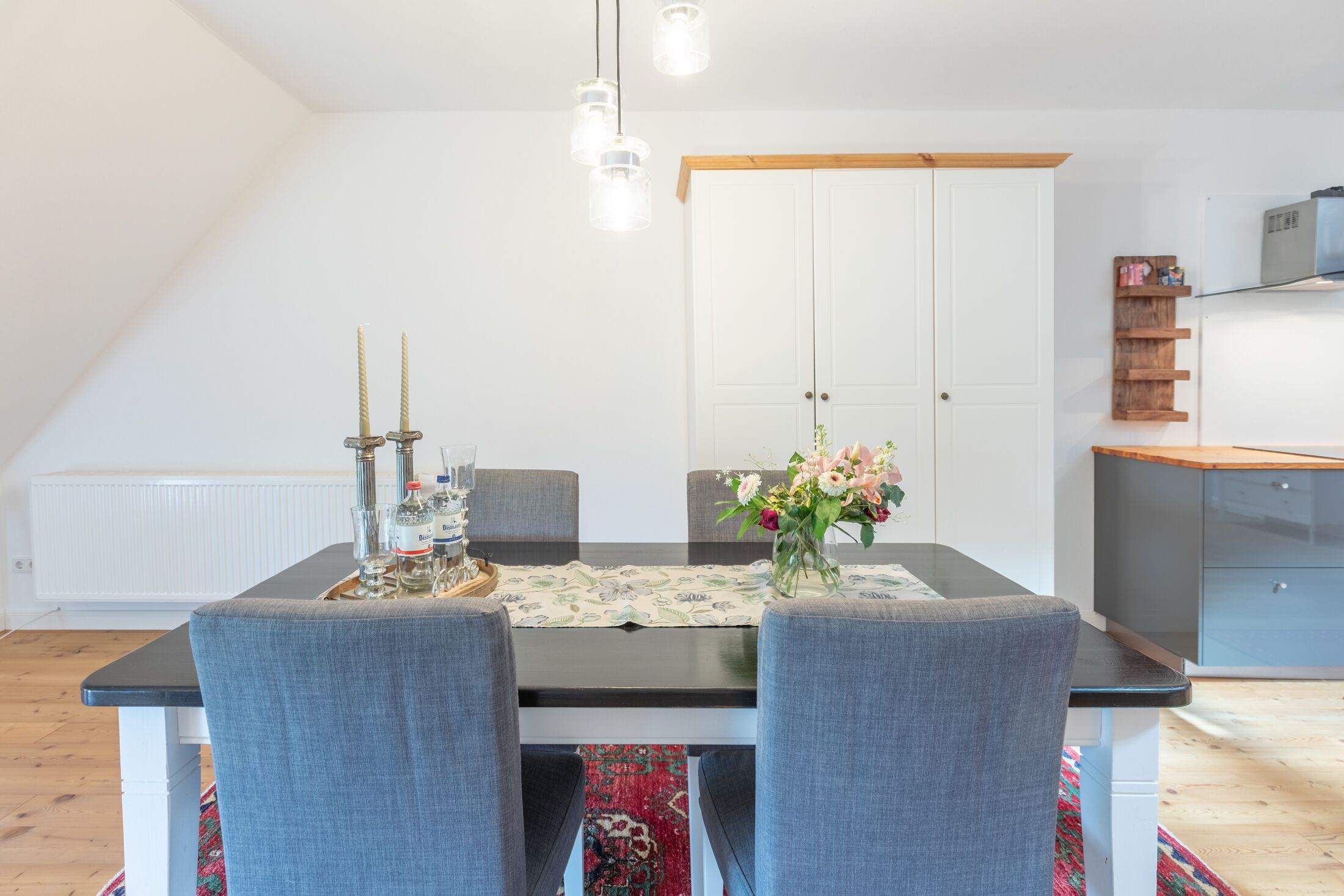 A dining area with a table set for four, a chandelier, and a cabinet with a shelf.