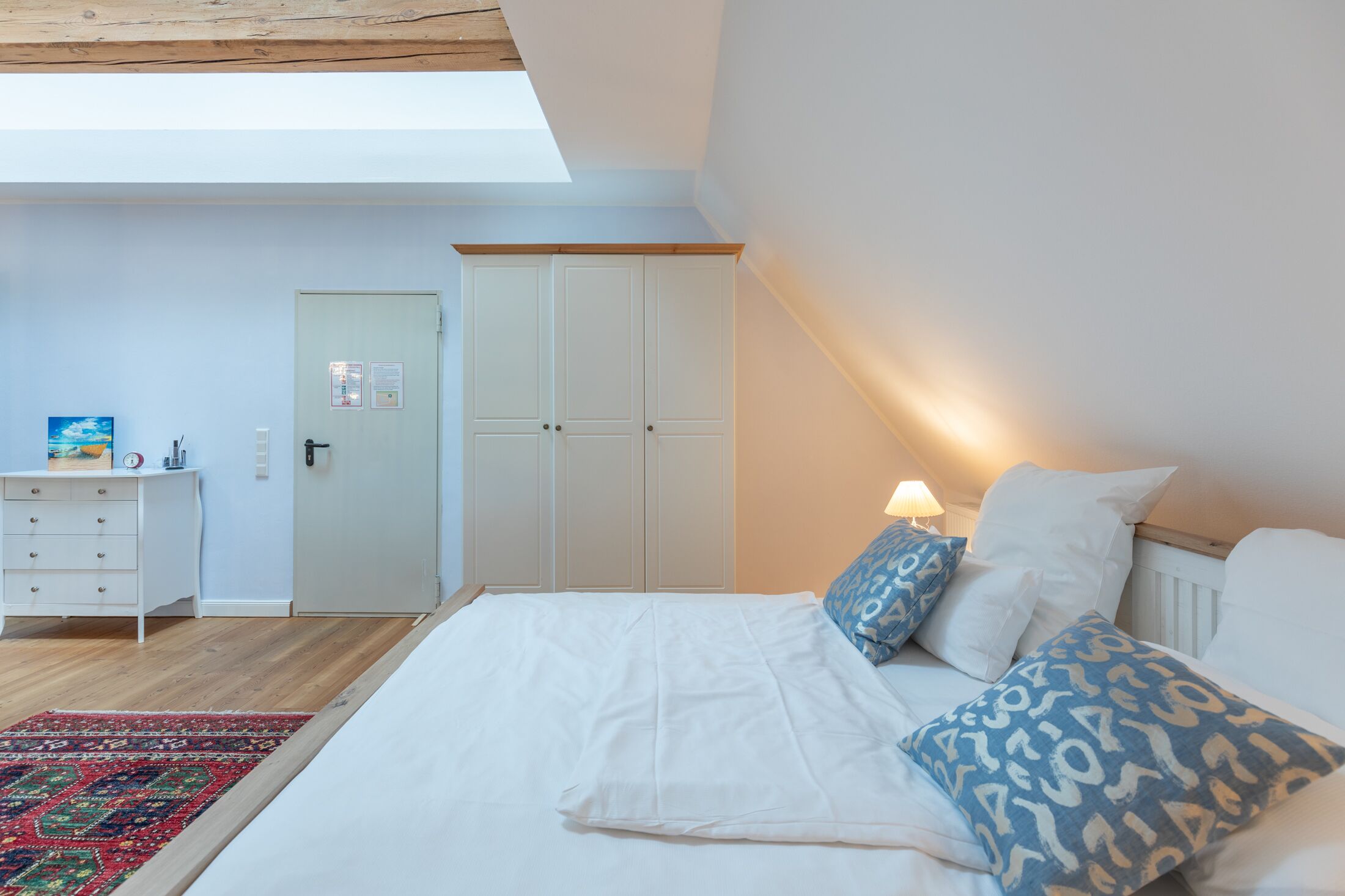 Quarto com cama grande, guarda-roupa, escrivaninha e claraboia.