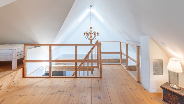 Quarto de sótão com pé direito alto, chão de madeira, um candelabro e uma cama.
